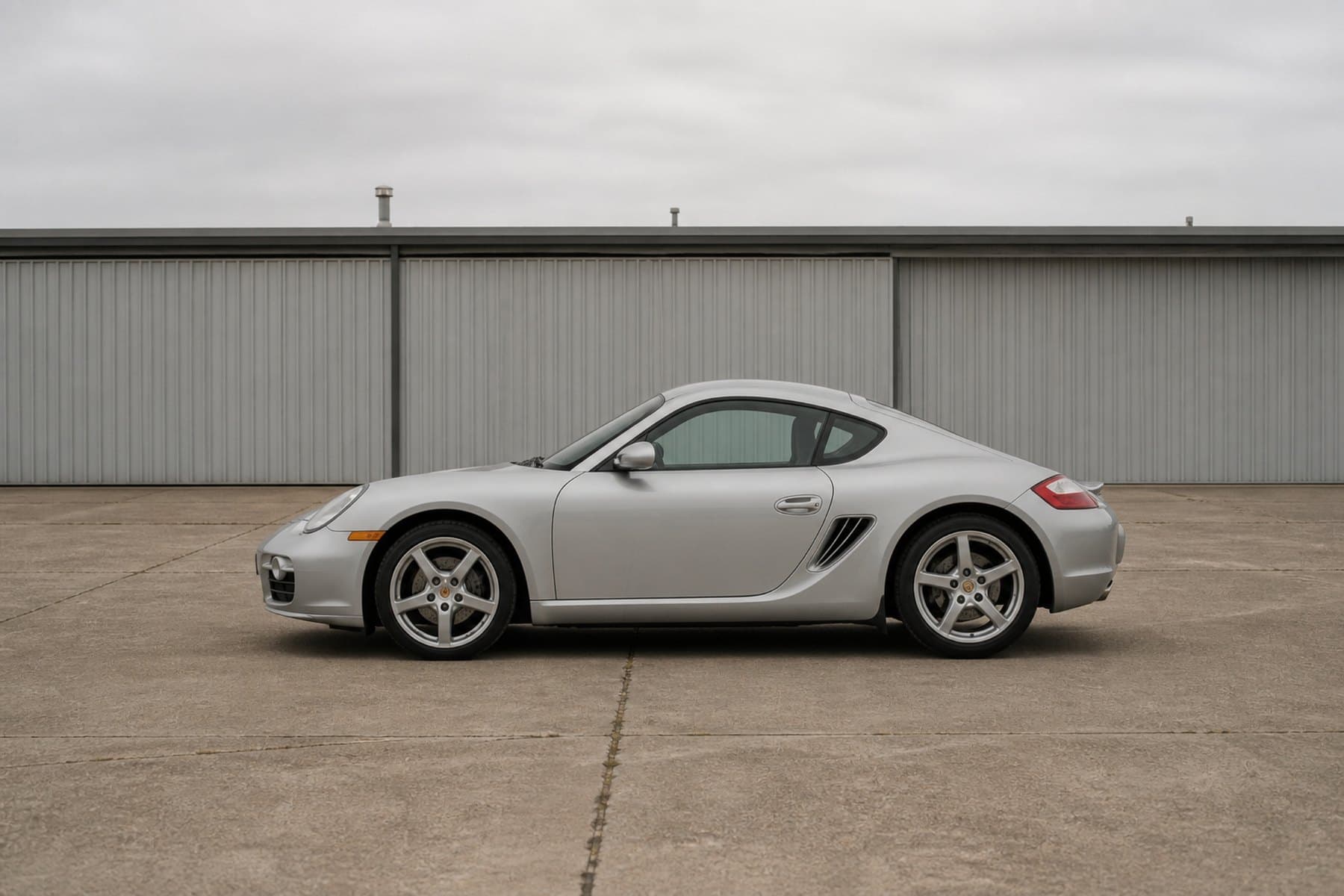 A silver Porsche Cayman parked beside a hangar