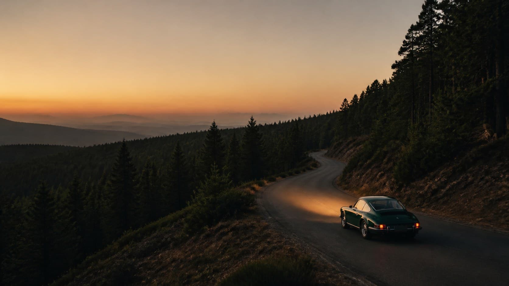 A dark green classic sports car climbing a winding forest road at dusk