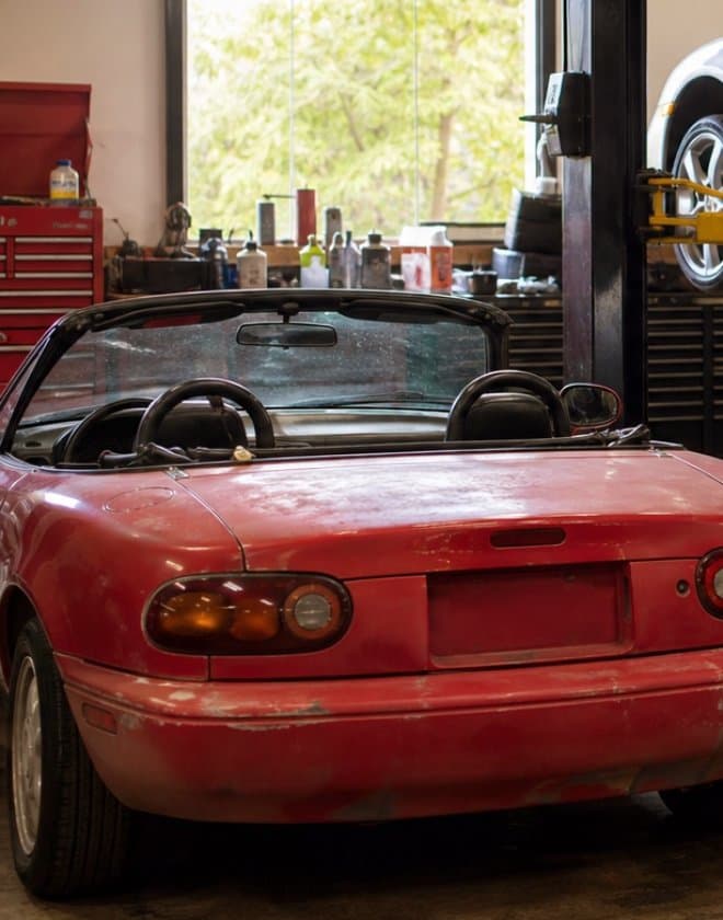 A well-worn red roadster parked in a home workshop